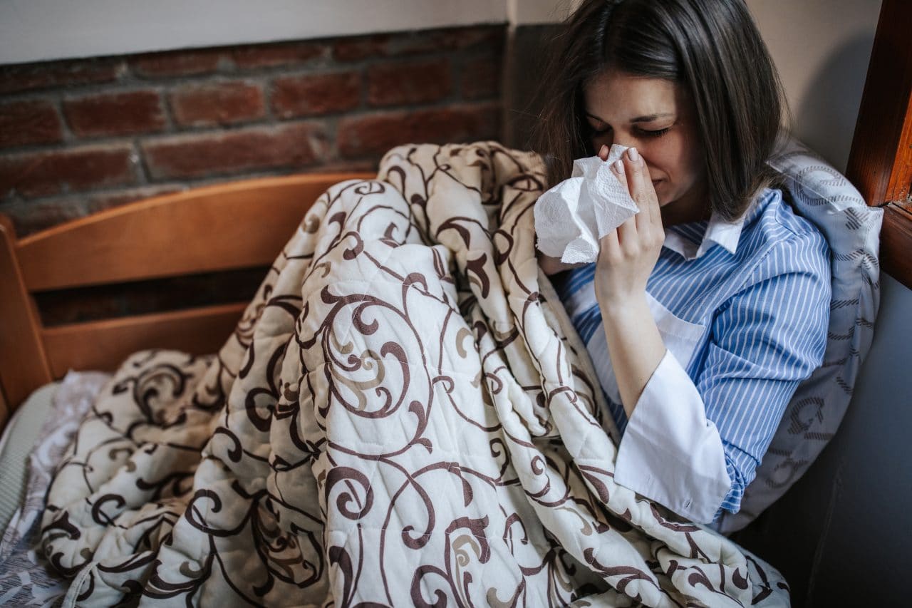 Woman sitting in bed with a tissue.