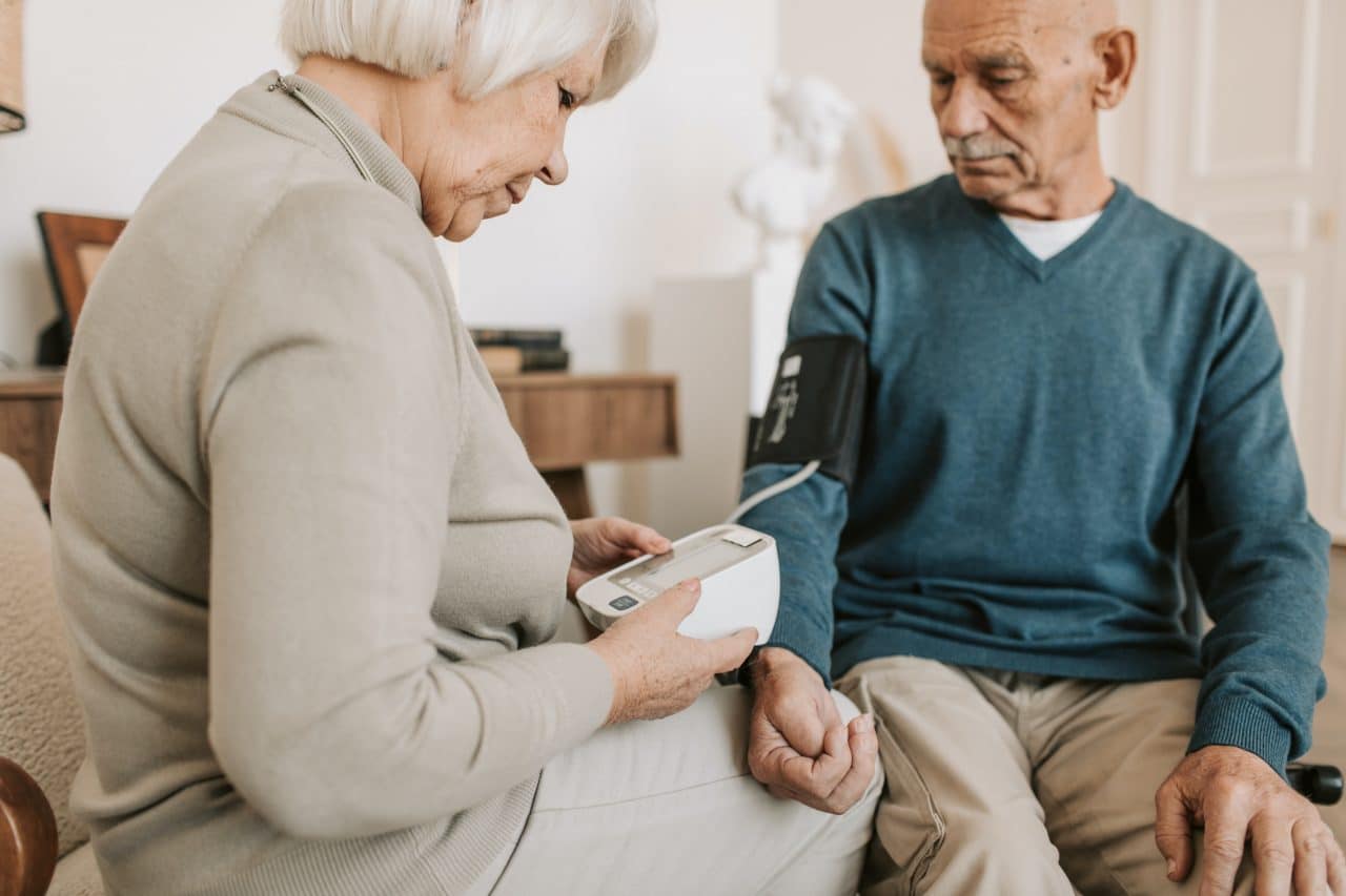 Wife helping her husband take his blood pressure with an at-home monitor.