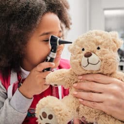 Girl plays with her toy bear in a medical game, using an otoscope. Hearing clinic for children